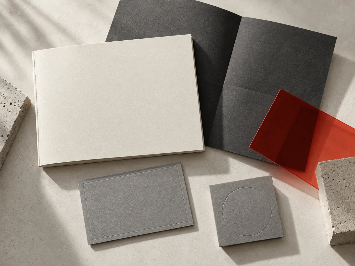 Editorial arrangement of cream books, charcoal paper and coral acrylic